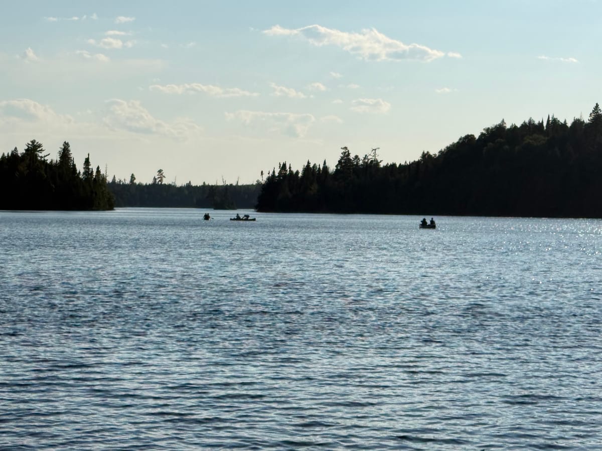 Two canoes crossing open water between forested points in the Boundary Waters