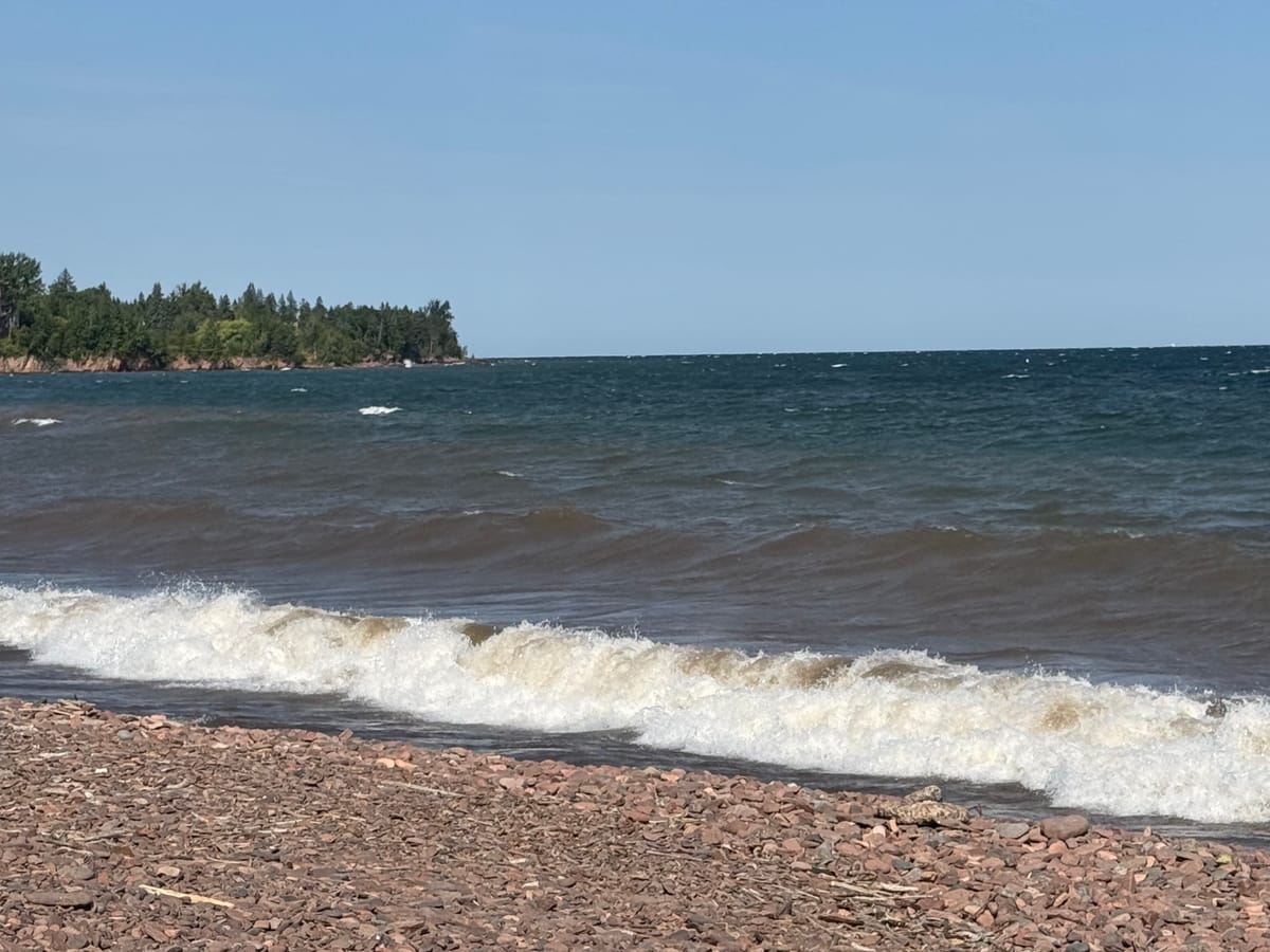 A wave breaking on the cobble beach of Lake Superior at Duluth, Minnesota, with a wooded headland beyond