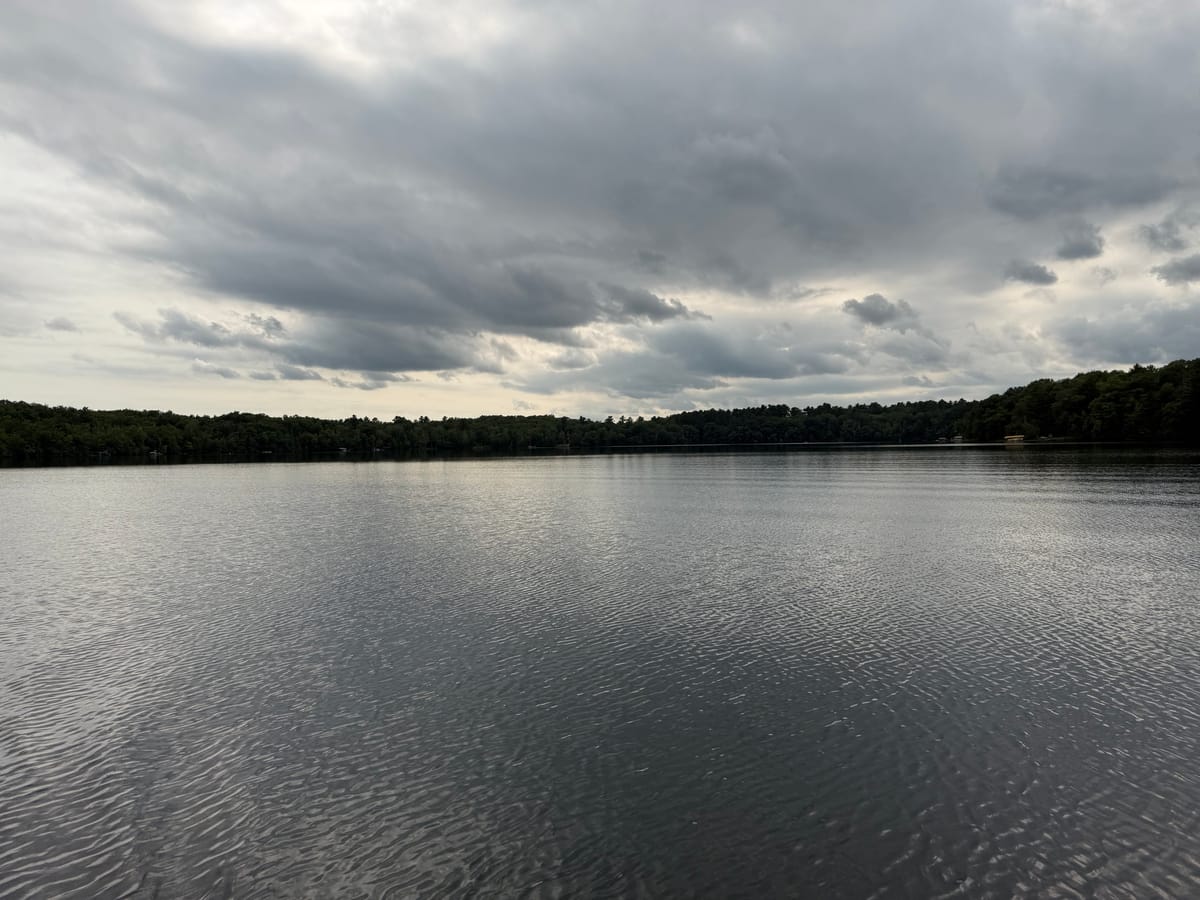 Slim Lake under flat overcast, dark open water running to a low wooded shore
