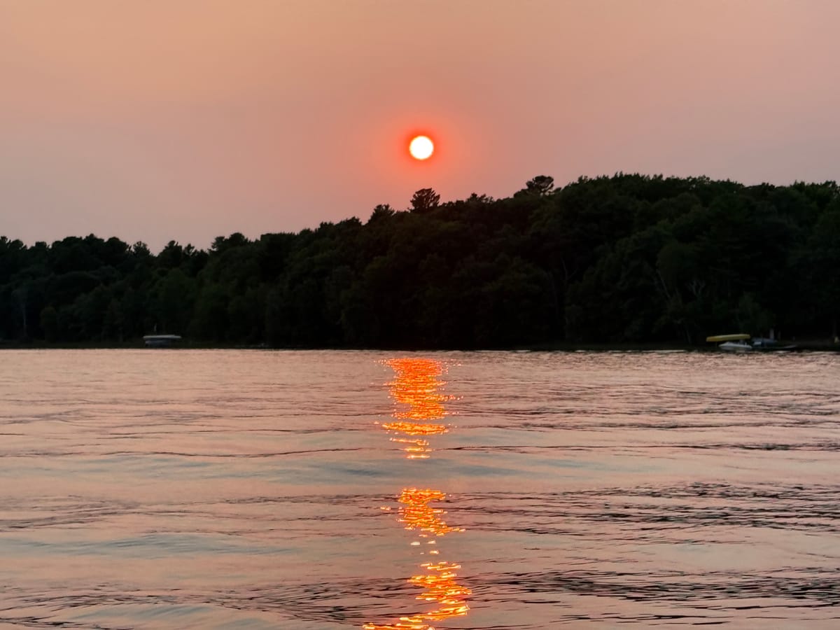 A red sun low over Slim Lake through wildfire haze, its reflection a column of orange on the water