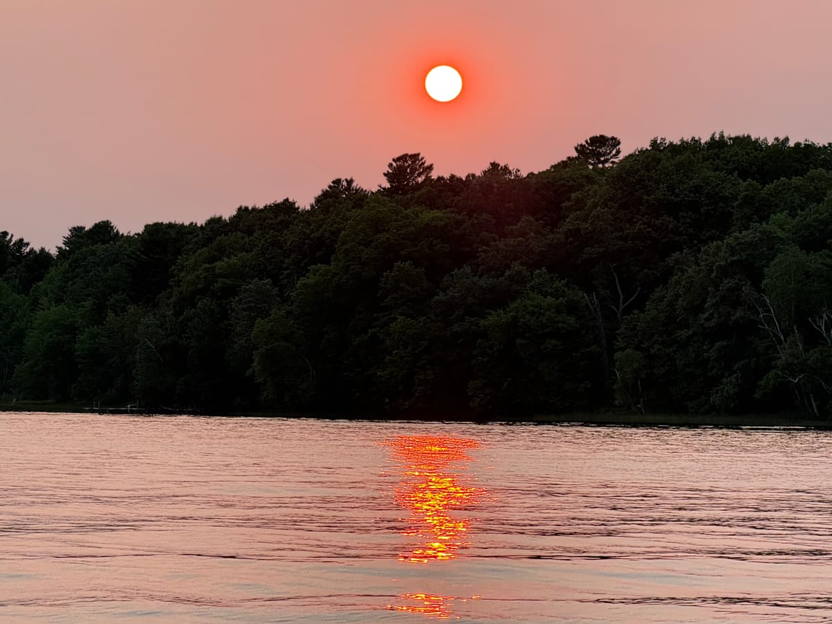 Wildfire smoke turning the setting sun deep red above the treeline on Slim Lake