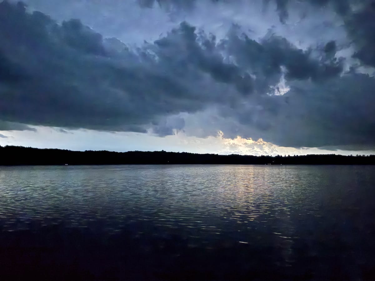A storm cloud deck moving over Slim Lake at dusk, the last light breaking through low on the horizon